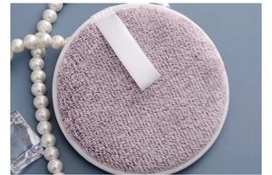 Macro detail of purple charcoal fiber makeup remover puff with white silk ribbon handle