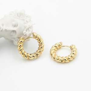 Detailed shot of gold-plated twisted hoop earrings next to a classic white sculpture