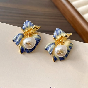 Dettaglio di orecchini vintage a fiore con smalto blu e perle a foglia d'oro