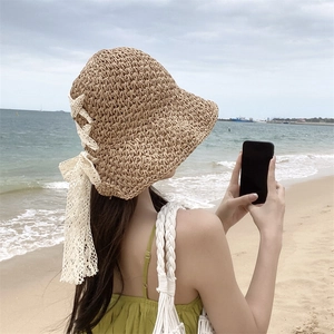 Women's foldable straw hat with white lace bow on beach background for sun protection