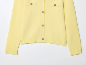 Detail of yellow knit cardigan featuring gold textured buttons and ribbed pockets