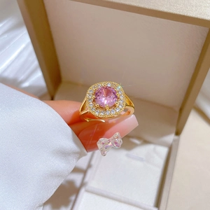 Close-up of gold ring with pink round gemstone and zircon accents on an open band