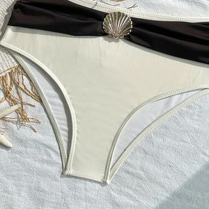 Close-up of off-white bikini bottom featuring a gold shell buckle and black pleated waistband