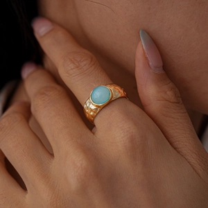 Vue macro d'une bague dorée texture lave ornée d'une pierre ovale de couleur bleu clair