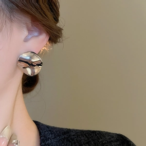 Detail shot of oversized irregular pleated silver earrings worn on a model's ear