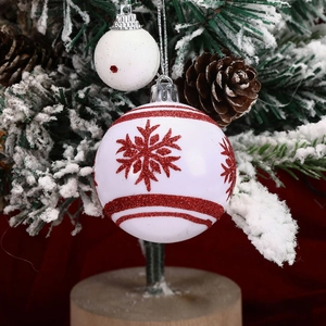 Close-up of white Christmas ball ornament with red glitter snowflakes on snowy tree