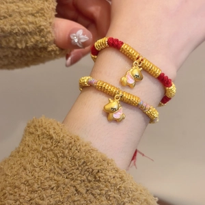 Close-up of woven red ropes with golden unicorn charms and pink enamel details