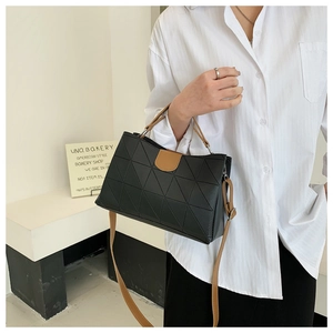 Detail of black geometric quilted handbag with brown contrast leather straps on a model