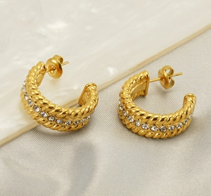 Detail view of U-shaped gold earrings with twisted texture and zircon inlay on marble