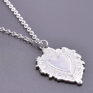 Macro detail of a vintage heart pendant with ornate scroll patterns and a metallic chain