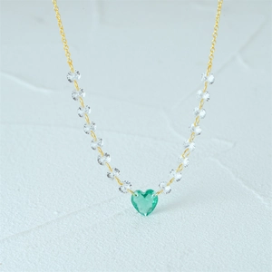 Macro shot of gold necklace with green heart-shaped crystal and white beads on dainty chain