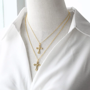 Collana a strati dorata con ciondolo a croce e zirconi su una camicia bianca