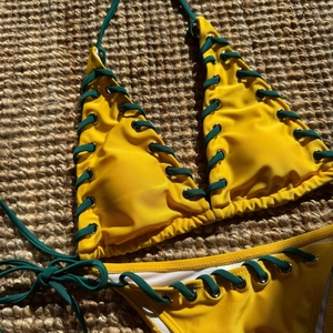 Detailed macro view of yellow bikini with dark green lace-up straps and metal eyelets