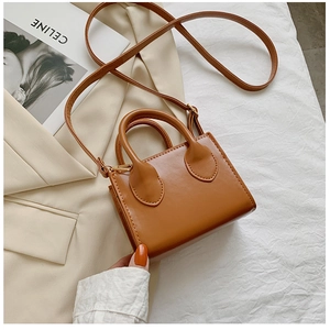 Detail of a brown leather mini square bag with round handles and crossbody strap on a model
