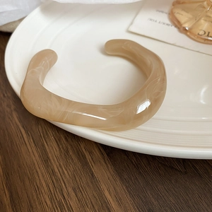 Detail of irregular acrylic cuff bracelet with beige marble texture on ceramic tray