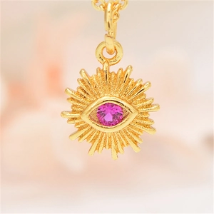 Macro shot of gold sun evil eye necklace pendant with a pink zircon stone inlay