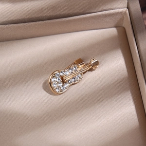 Détail d'une broche violon dorée avec strass dans un coffret à bijoux beige