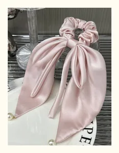 Detail of pink satin bow hair scrunchie with elegant pearl accents on ribbon ends