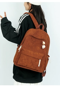 Detail eines braunen Cord-Rucksacks mit zwei Bären-Pins und seitlichen Tunnelzugtaschen