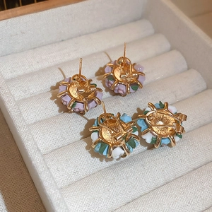 Macro detail of gold floral stud earrings with purple ceramic petals in a velvet jewelry box