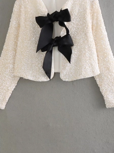Detail view of ivory sequin jacket featuring elegant large black satin ribbon bow closures