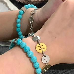 Dettaglio del braccialetto di perline blu e catena dorata con ciondoli lettere H e 7