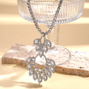 Silver hollow teardrop necklace with sparkling crystals on a textured glass vessel