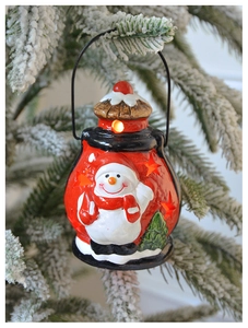 Lanterne de Noël rouge avec relief de bonhomme de neige blanc suspendue sur des pins enneigés