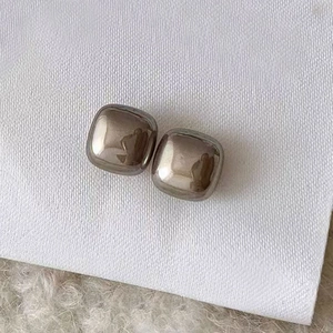 Close-up of minimalist polished square metal stud earrings on a textured white background