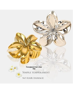Close-up of gold and silver metal plumeria flower hair claws on a reflective surface
