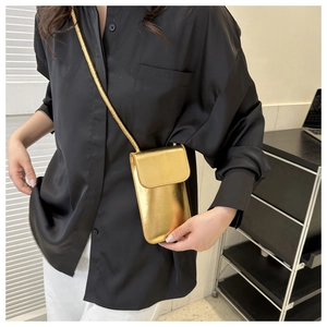 Detail einer glänzenden goldenen Handy-Mini-Tasche gestylt an einer schwarzen Seidenbluse