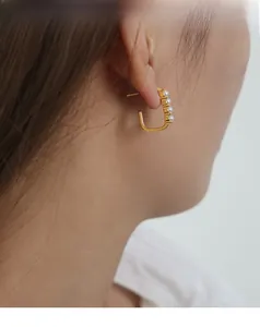 Close-up of C-shaped 18k gold plated earrings with five white pearls worn by model