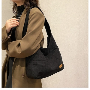 Detail view of black corduroy bucket bag with wide strap on shoulder of a model in suit