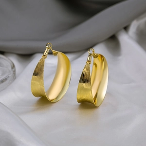 Exaggerated golden C-shaped hoop earrings with brushed texture on silk background