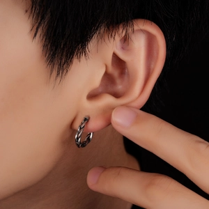 Close-up of a silver twisted hoop earring on a model ear with a vintage metal texture