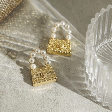 Detail view of mini quilted gold handbag earrings with pearl handles and logo