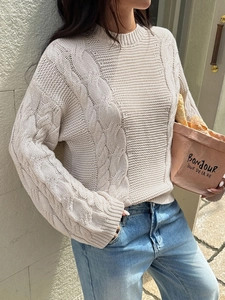 Detailed knit texture of a beige cable knit sweater styled with casual denim jeans