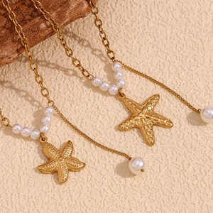 Close-up of 18K gold-plated double-layer necklace with starfish and faux pearls on sand