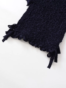 Macro detail of navy textured smocked fabric with ruffle hem and delicate side ties