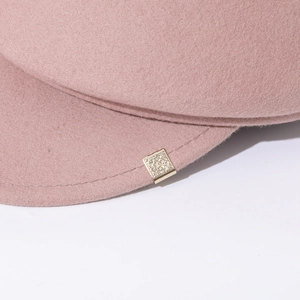 Detail of pink wool newsboy hat featuring an ornate gold square metal buckle on brim