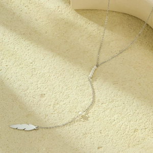 Long stainless steel necklace with leaf pendant and pearls on a beige stone surface