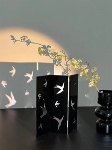Detail of black acrylic folding screen with bird cutouts and artistic light shadows