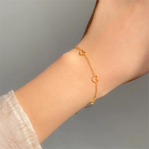 Close-up of gold heart charm bracelet on wrist featuring minimalist openwork design