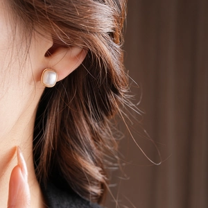 Macro shot of square gold-rimmed pearl earrings worn by a model in soft lighting