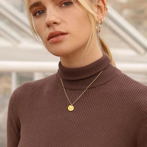 Detailed view of a gold circular butterfly pendant necklace on a brown turtleneck sweater
