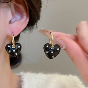 Detailed close-up of gold hoop earrings with black enamel heart pendant and rhinestones