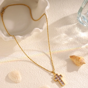 Macro shot of gold cross necklace with square zircons and twisted chain on sand