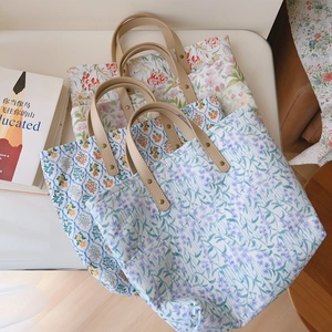 Trois sacs cabas en coton à fleurs avec poignées en cuir empilés sur une table blanche