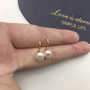 Detailed view of white freshwater pearl earrings on gold hooks held for size reference