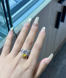Detail of leaf-shaped silver ring featuring a yellow pear-cut zircon on a model's hand